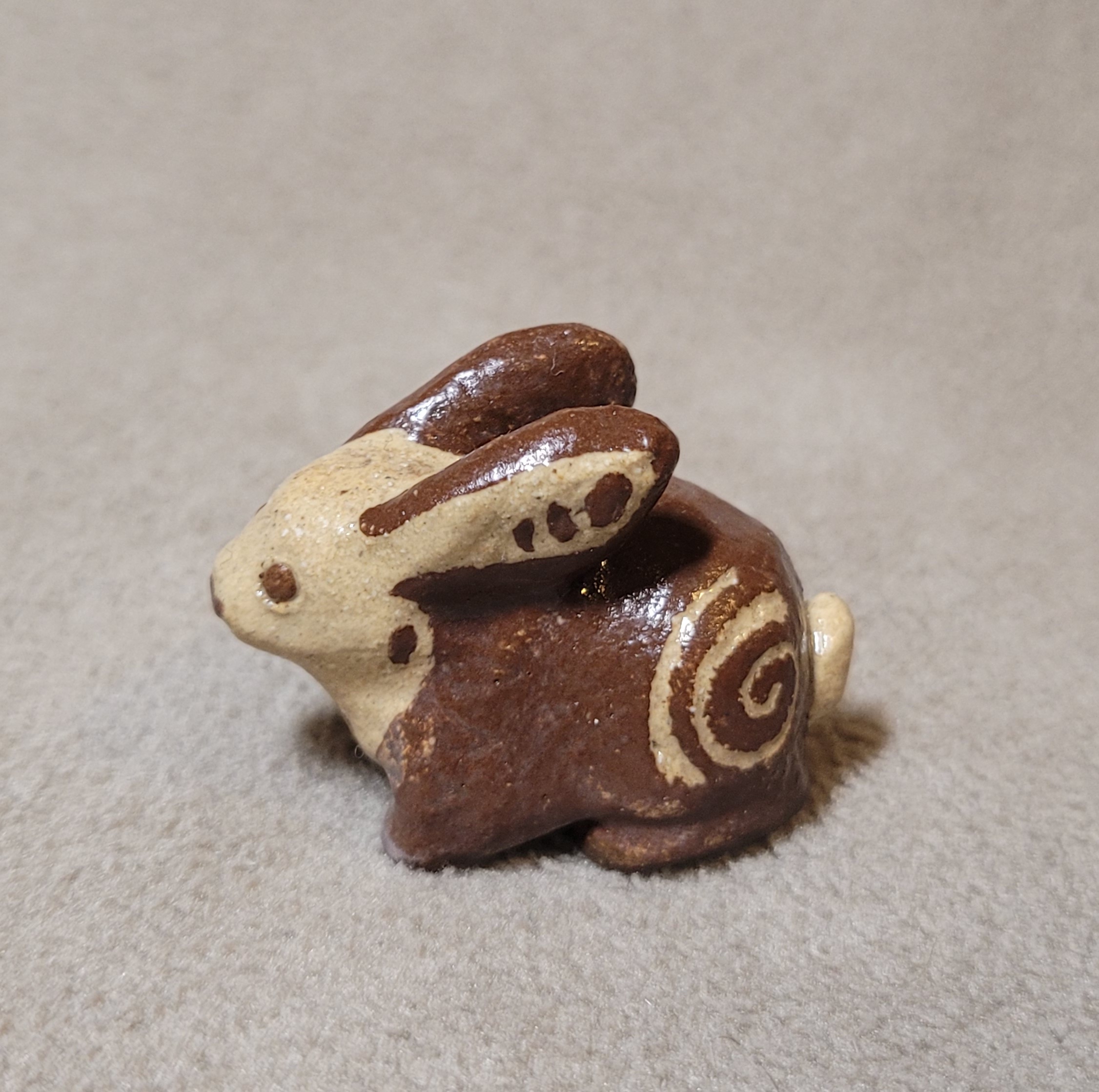 Brown and cream colored ceramic rabbit with a cream spiral on its haunch