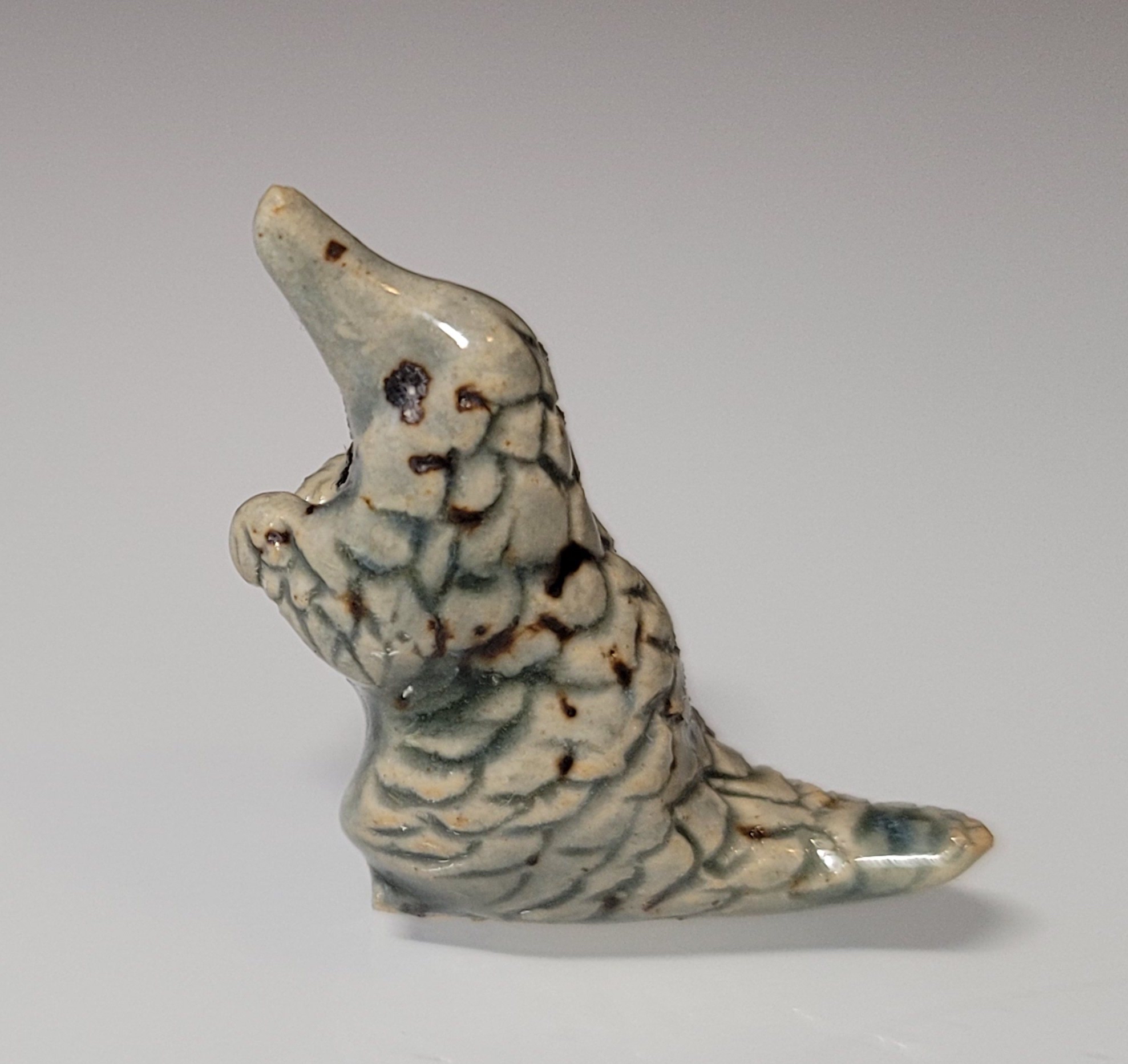 Tiny green ceramic pangolin standing up on its hind legs with paws raised as if pleading